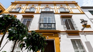 A building with a white facade and yellow trim, featuring multiple windows with metal bars, a central large window, and a door with a number plaque. - San Lorenzo 5 - One Bedroom Apartment, Sleeps 4 (Sevilla)