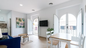A modern living room with a sofa, a dining table with chairs, a TV mounted on the wall, and a balcony with a railing. - San Lorenzo 5 - One Bedroom Apartment, Sleeps 4 (Sevilla)