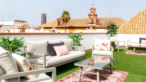 An outdoor seating area with white furniture, a glass table, and a patterned rug.