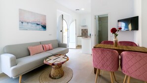 A modern living room with a grey sofa, a round coffee table, and a dining area with a wooden table and pink chairs.