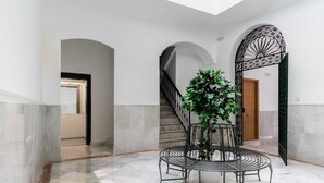 A spacious lobby with a marble floor, a central round table with chairs, and a staircase with a decorative metal railing.