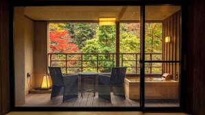 A room with a view of autumn trees through a large window, a small table with chairs, and a hot tub. - Shionoyu Onsen Rengetsu (Nasushiobara)