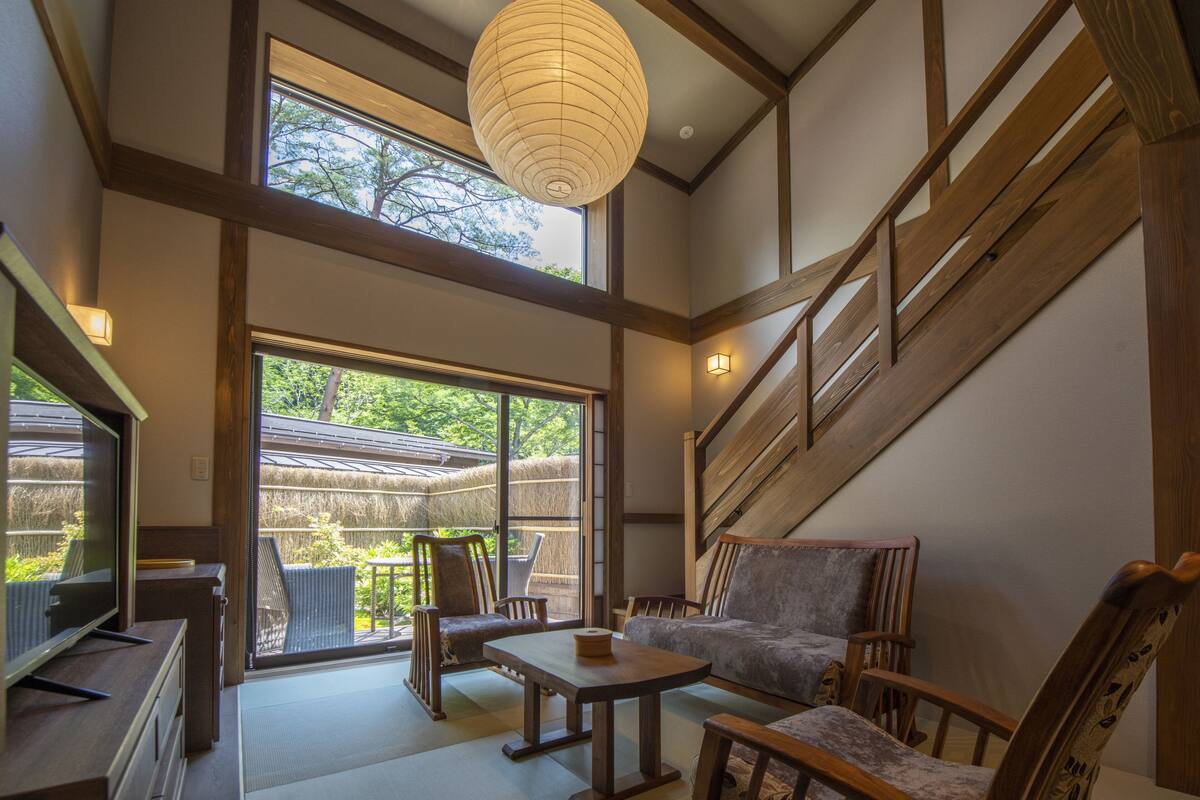 A spacious room with a large sliding glass door leading to a balcony, wooden furniture, and a traditional Japanese lantern.