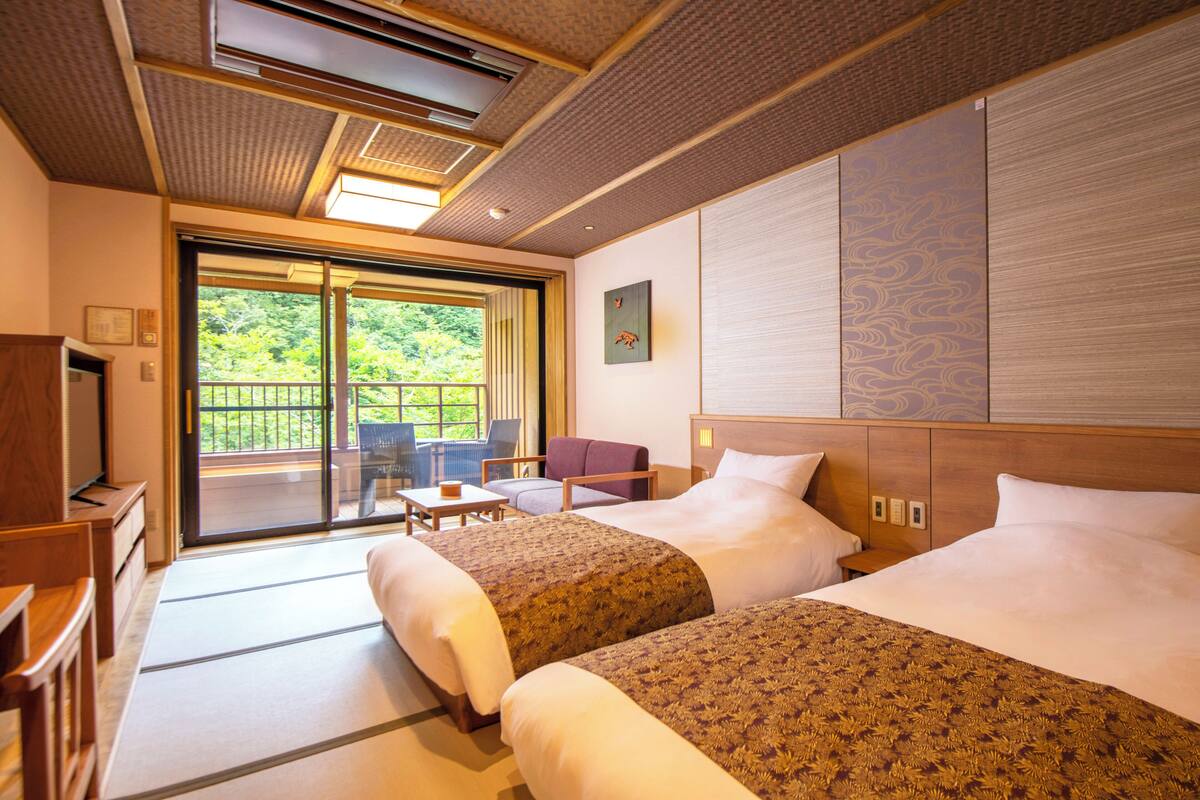 A hotel room with two beds, a balcony with a view, a small table, and a chair.