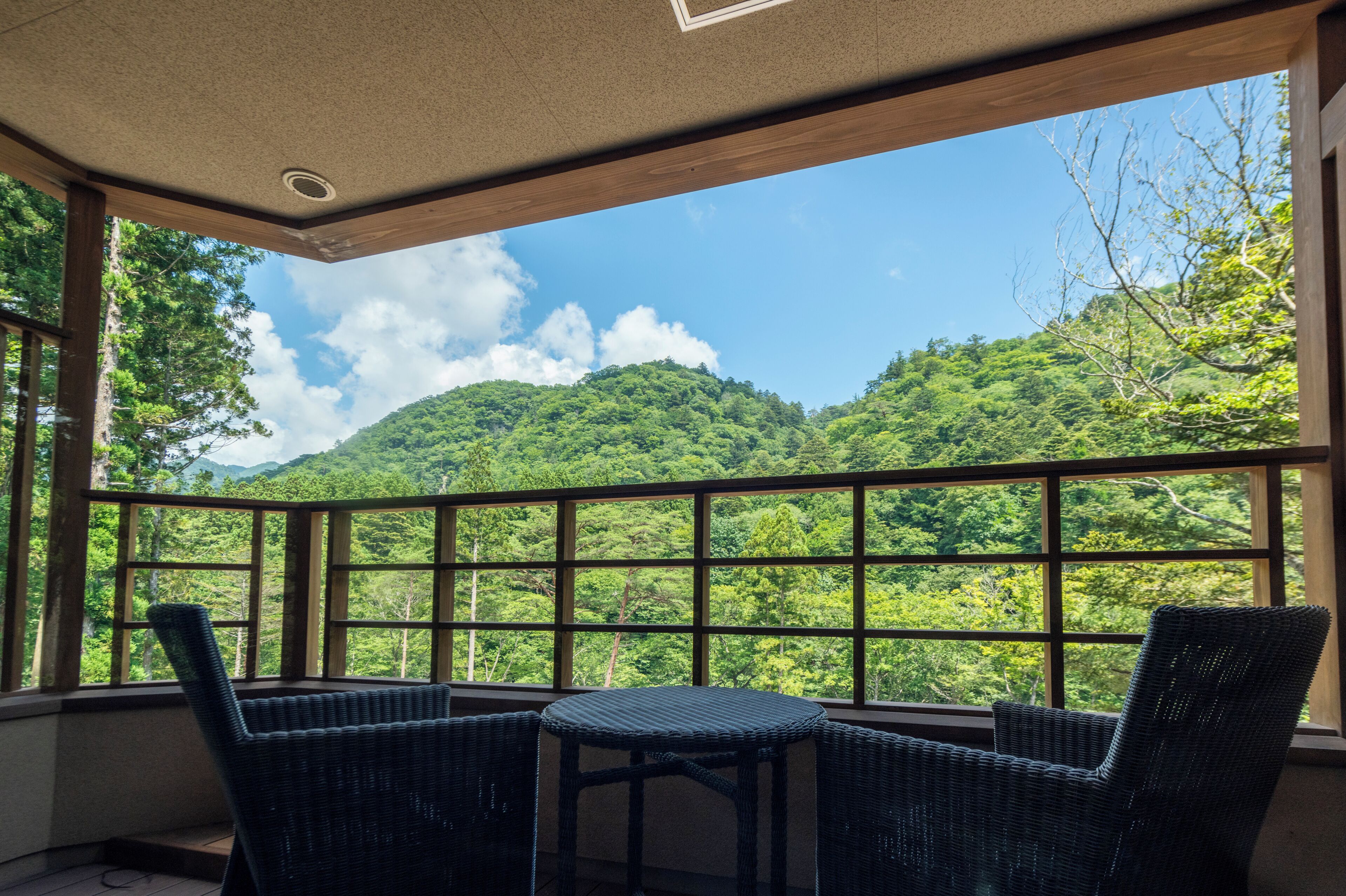 A room with a view of a forested mountain, wicker furniture, and a ceiling with a recessed light.