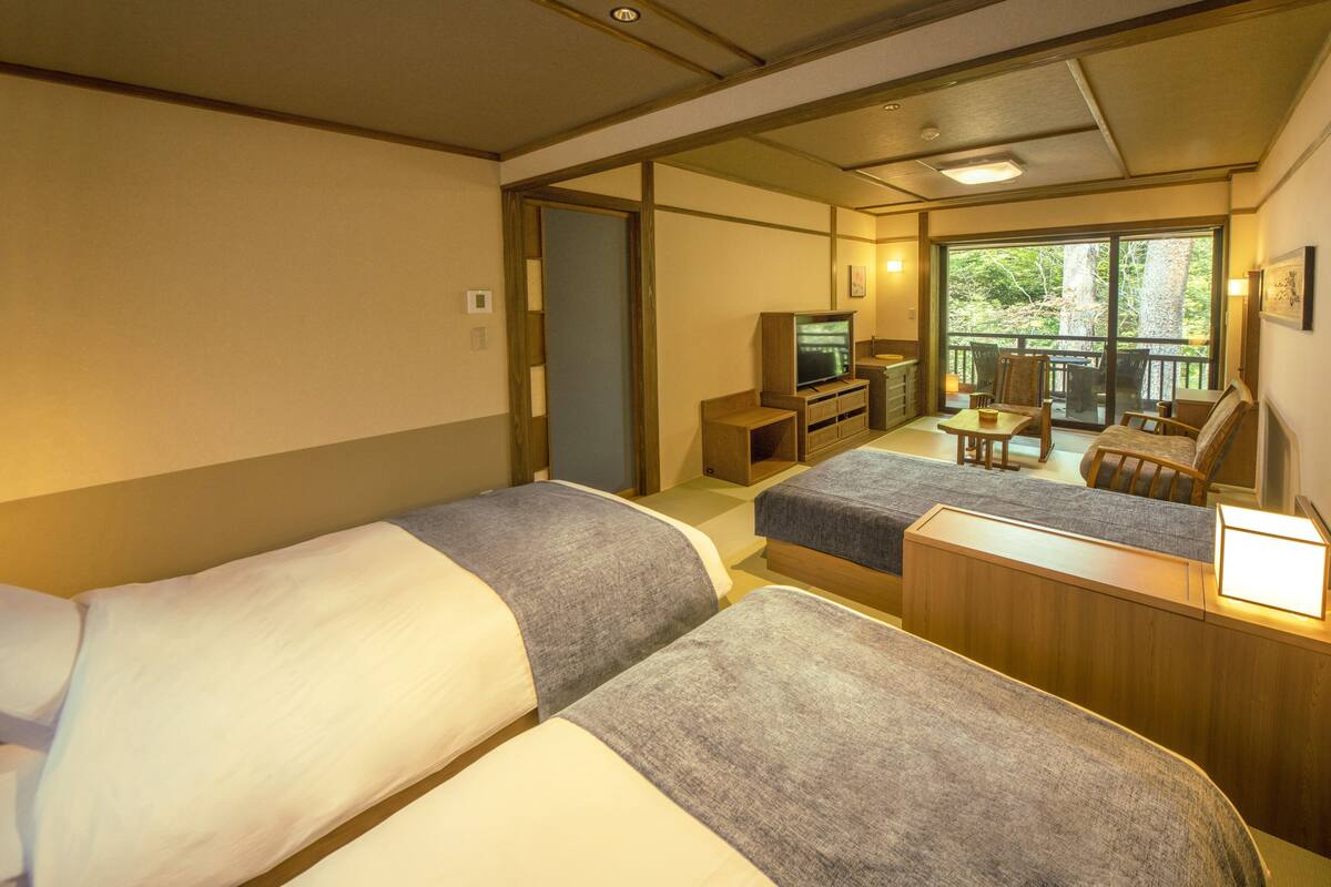 A hotel room with two beds, a TV, a small desk, and a balcony with chairs and a table.