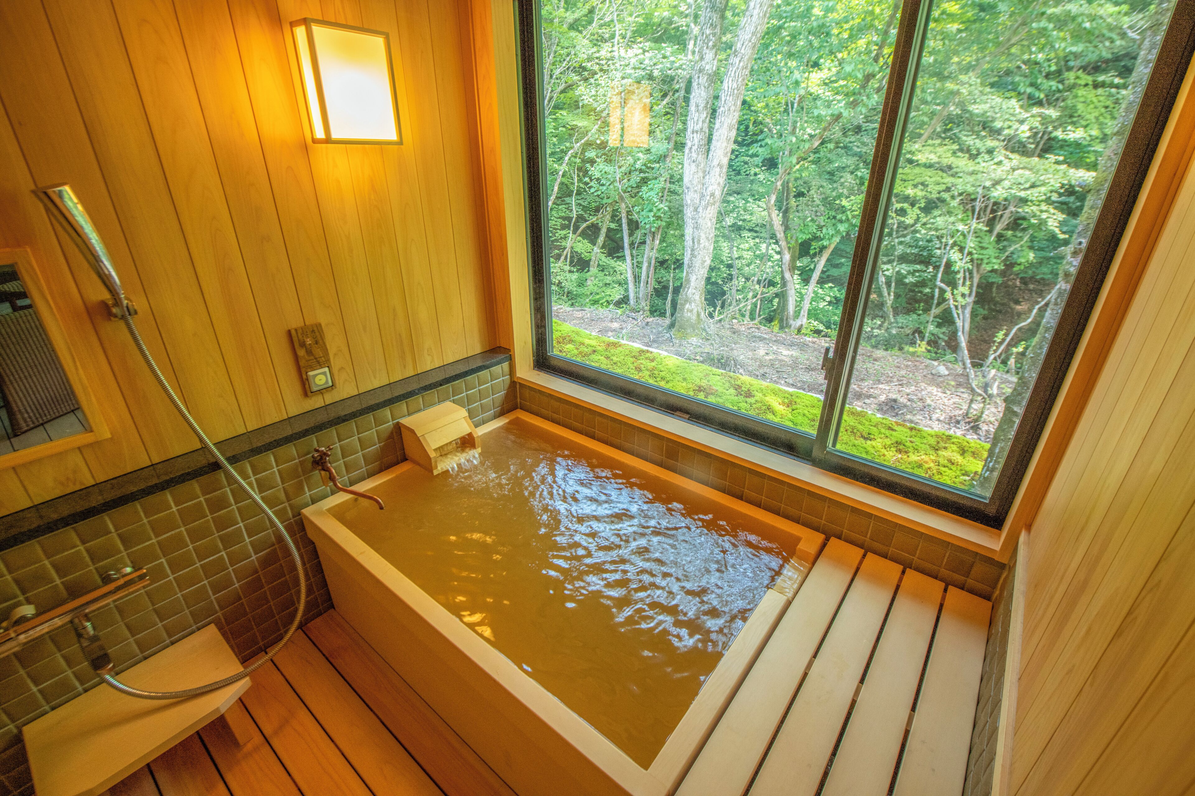 A wooden interior with a large bathtub, a window with a forest view, and a shower area.