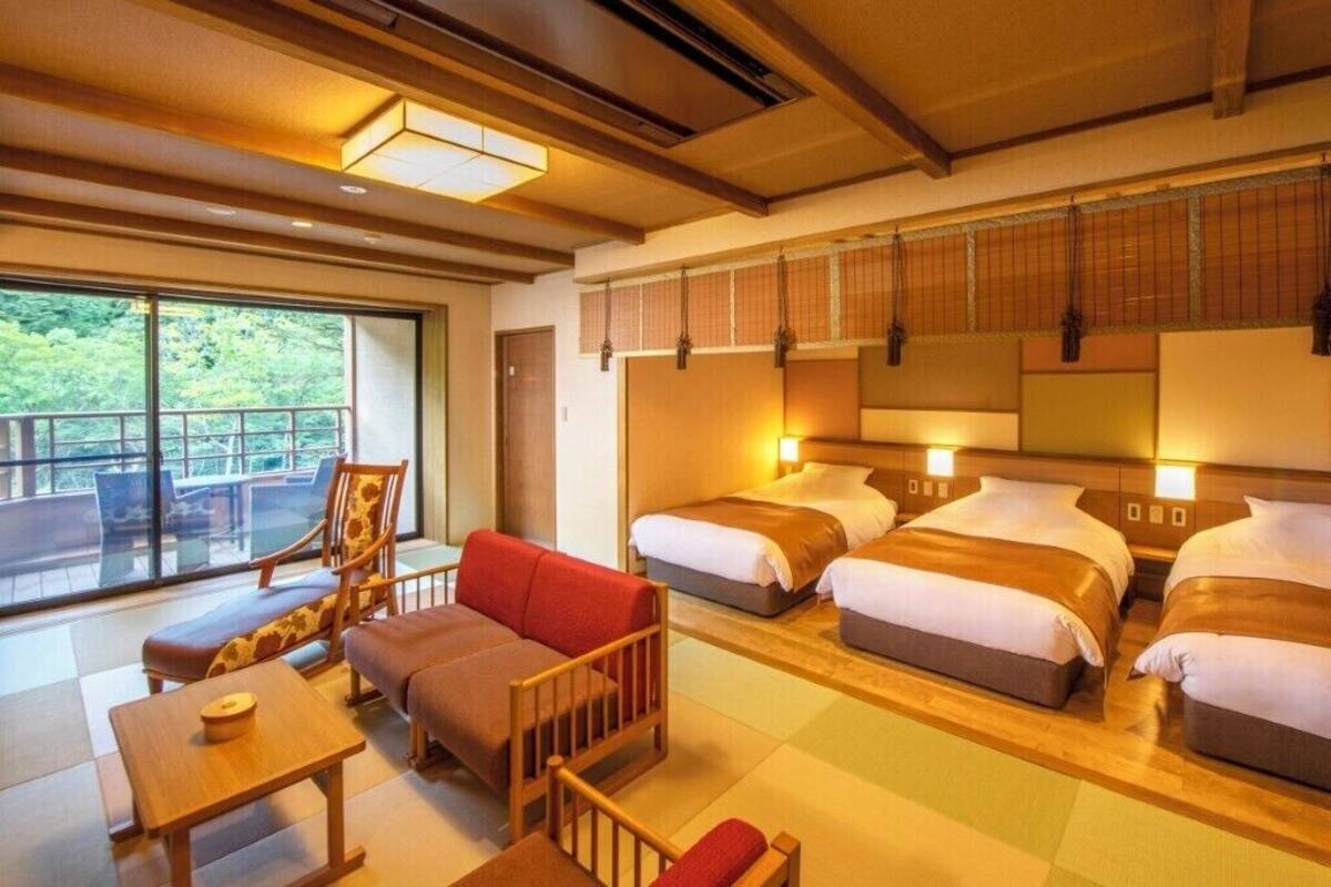 A hotel room with a balcony, two beds, a sofa, a small table, and a chair.