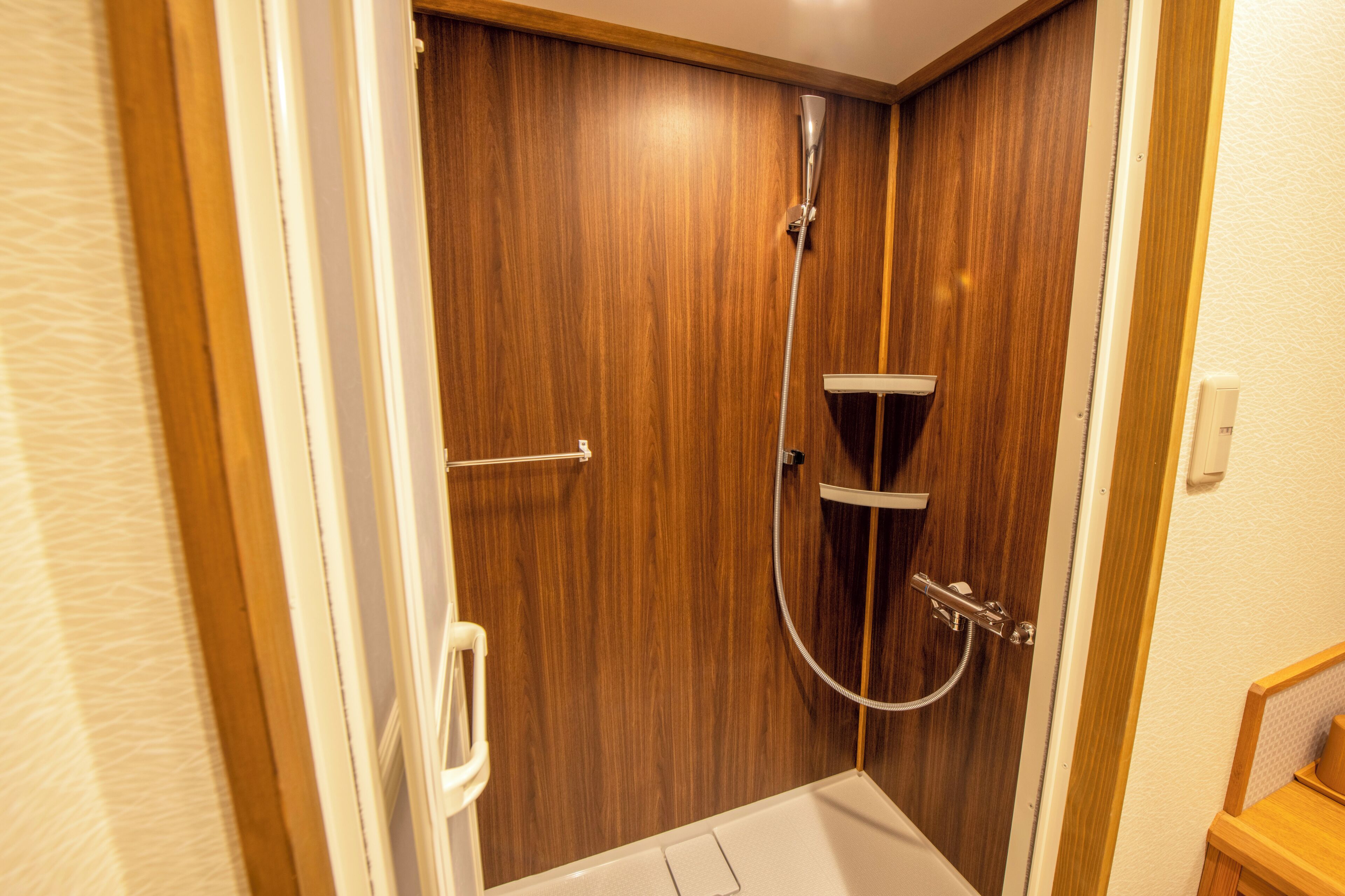 A small, enclosed shower area with a wooden door, a handheld showerhead, and a white bathtub.