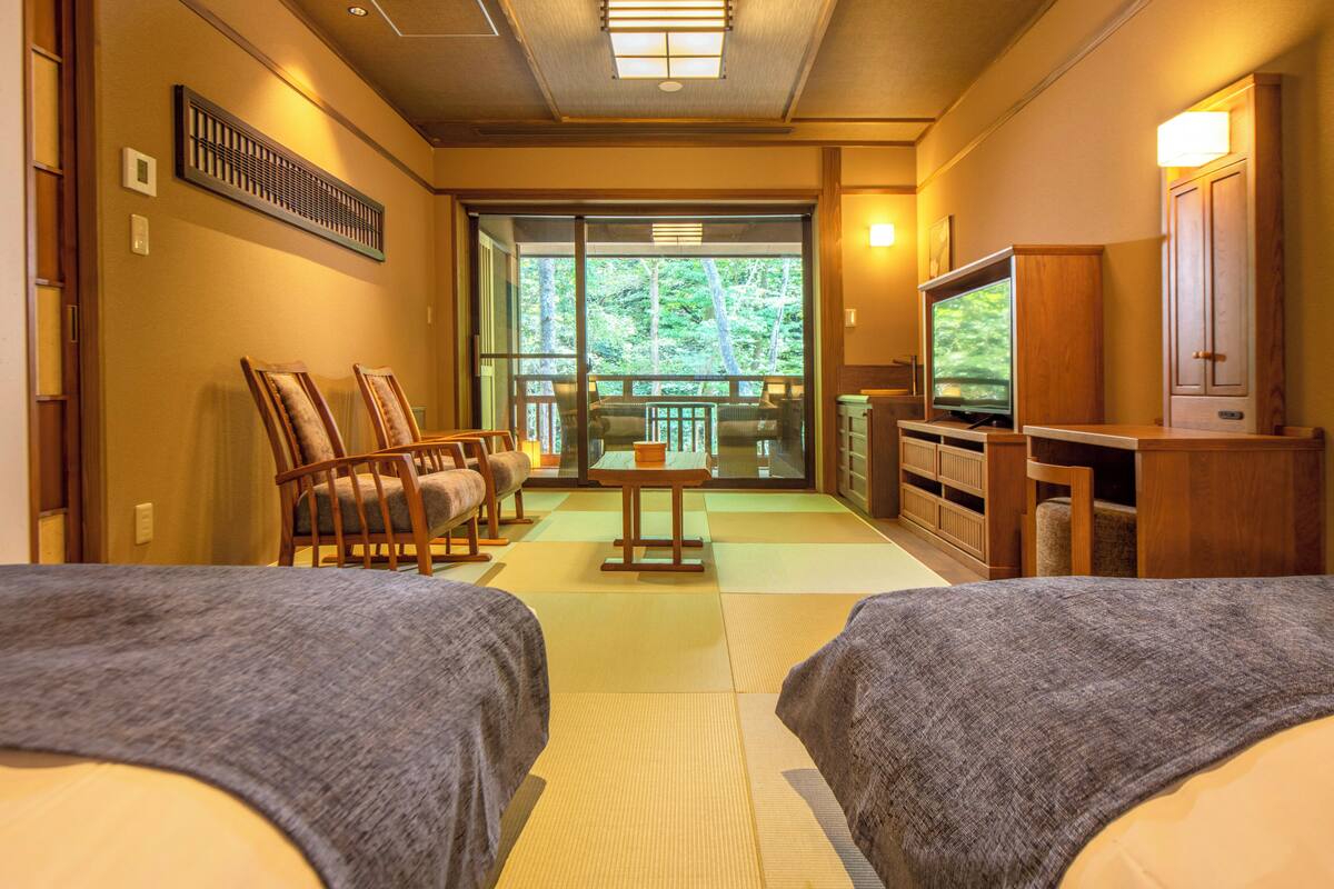 A hotel room with two beds, a television, a seating area with chairs, a table, and a view of the outdoors.