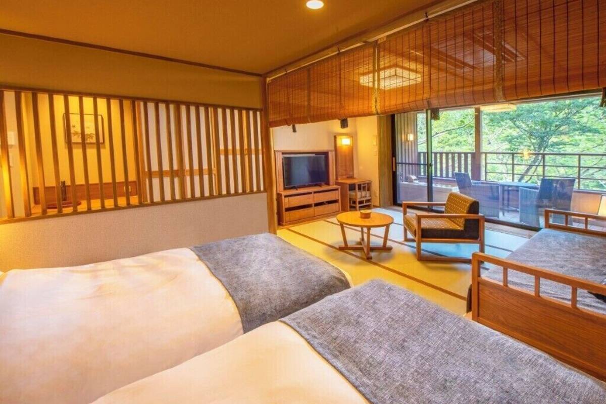 A hotel room with two beds, a TV, a small table, and a balcony with seating.