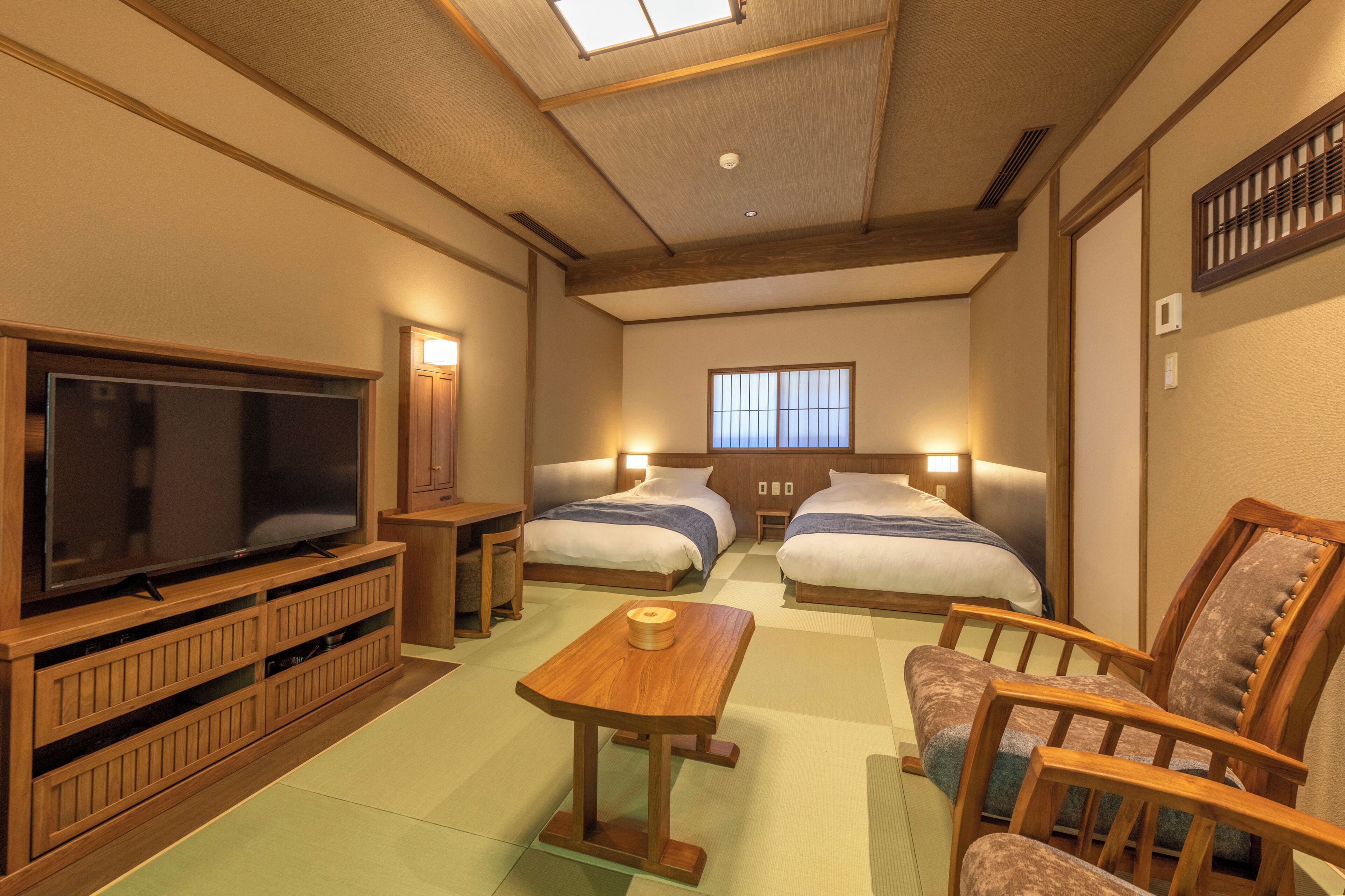 Una habitación de hotel con televisión, dos camas, una mesa de madera y una silla.