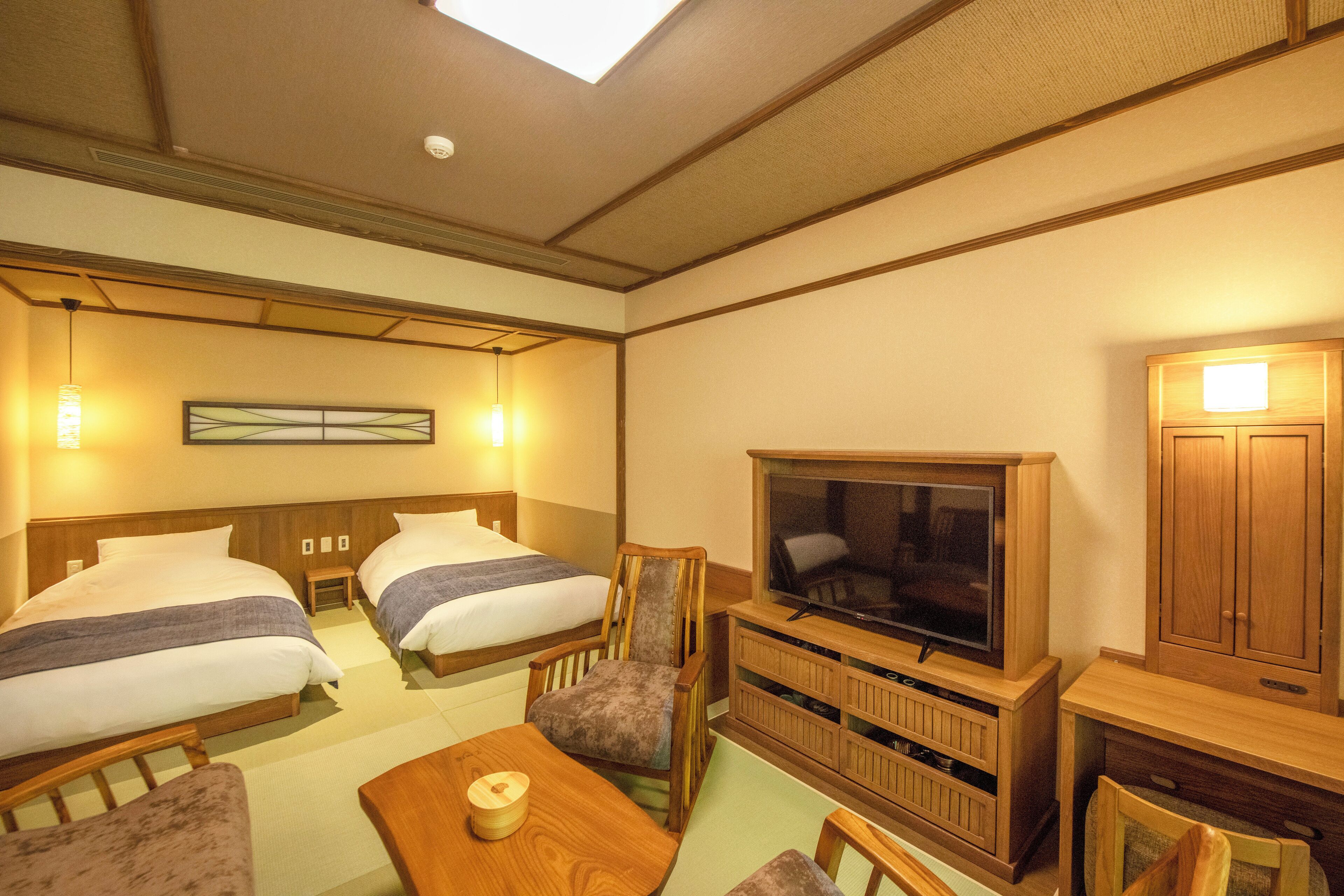 A hotel room with two beds, a television, a wooden cabinet, and a small table.