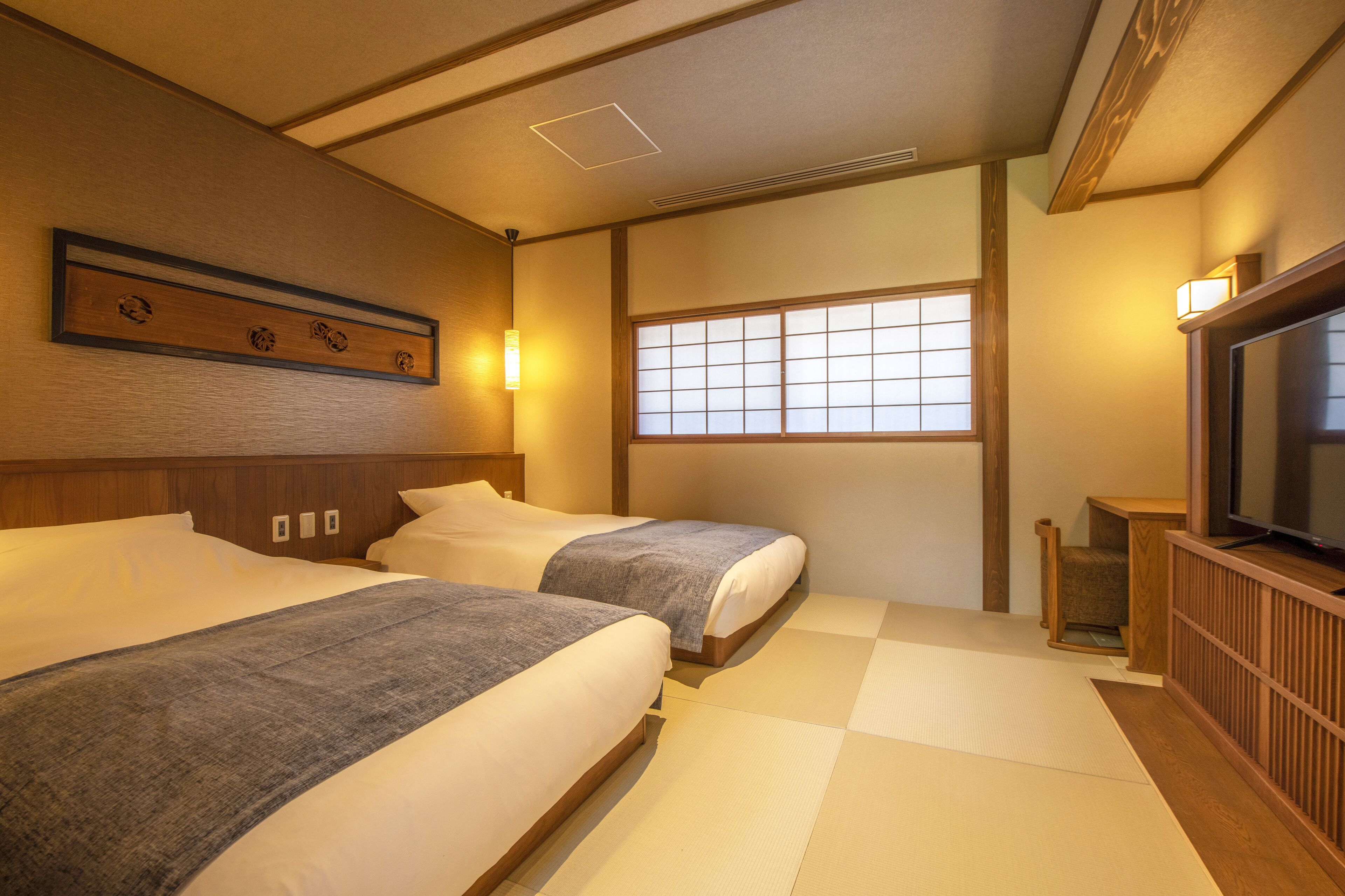 Een traditionele Japanse hotelkamer met tatami vloeren, twee bedden, een televisie en een raam met een shoji scherm.