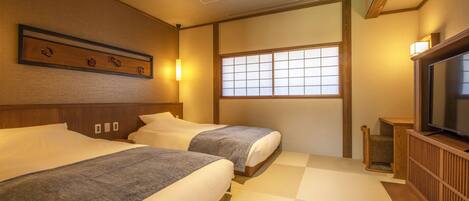 Habitación de hotel al estilo japonés tradicional con suelo de tatami, dos camas, televisión y ventana con celosía shoji.