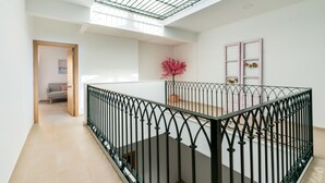 Un interior espacioso con techos altos, una escalera con barandilla de hierro forjado y vistas a una habitación con un árbol rosado.