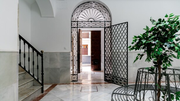 Un pasillo con suelo de mármol, una escalera, un arco decorativo y una planta en maceta.