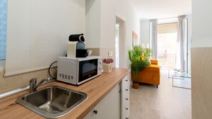 Eine moderne Küche mit Spüle, Mikrowelle und Kaffeemaschine. Im Wohnbereich befindet sich ein Holztisch und eine Pflanze.