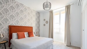 Ein Schlafzimmer mit einem großen Bett, einem Nachttisch, einer Lampe, einem Wandpapier mit Muster, einer Pendelleuchte und einem Fenster mit Vorhängen.