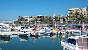 A marina with various boats docked, surrounded by buildings and palm trees.
