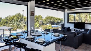 Un espace de repas extérieur moderne, doté d’une grande table pouvant accueillir six personnes, d’un coin salon confortable avec des canapés et d’un téléviseur.