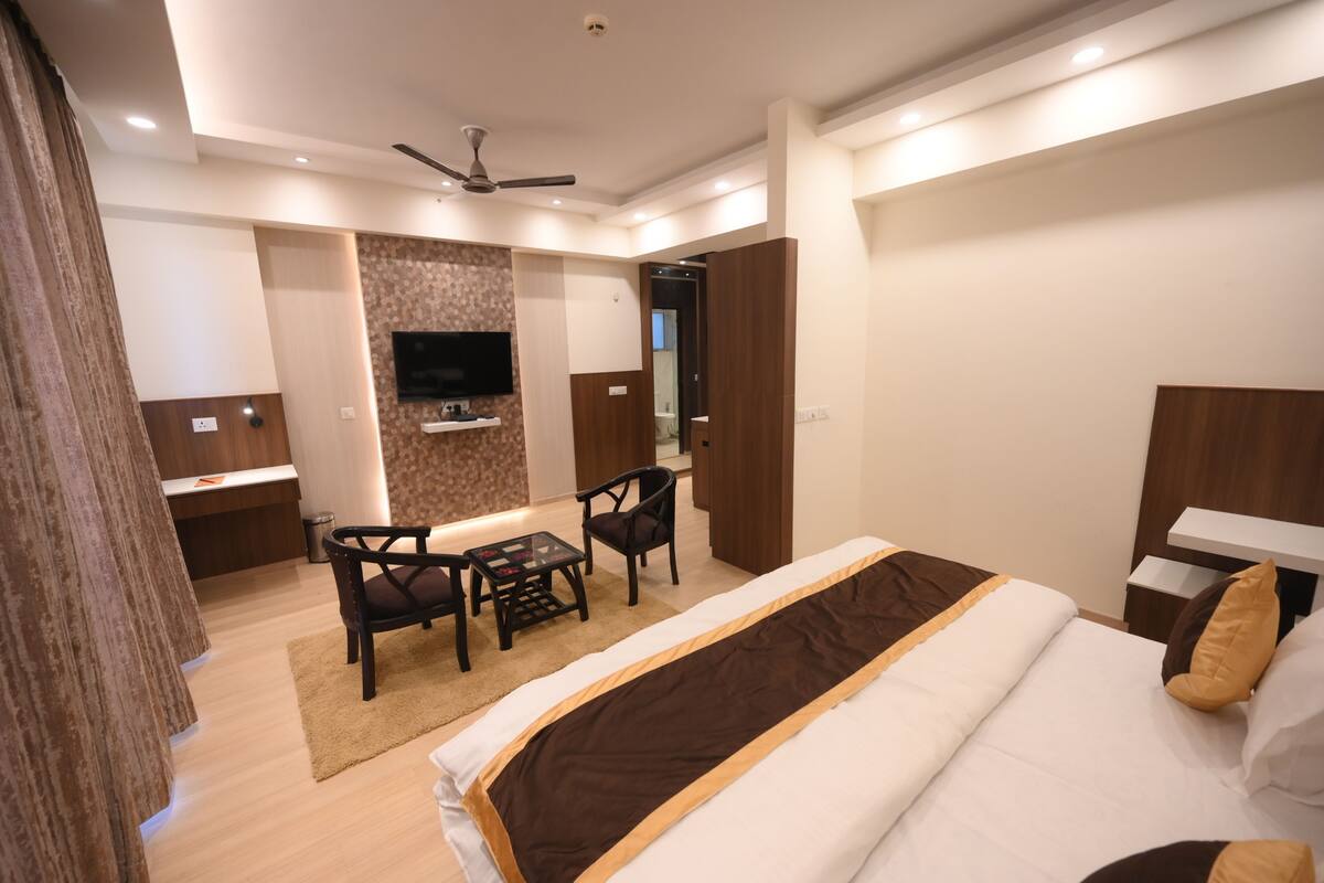 A hotel room with a bed, a desk with a chair, a television, and a ceiling fan.
