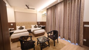 A hotel room with two beds, a ceiling fan, a small table, two chairs, and a large curtain. - Fairvacanze Inns & Suites Lucknow (Lucknow)