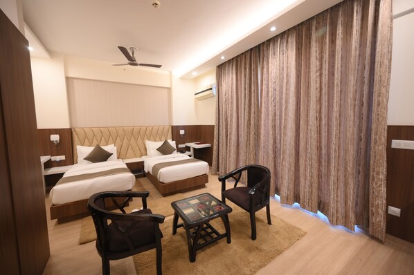 A hotel room with two beds, a ceiling fan, a small table, two chairs, and a large curtain.