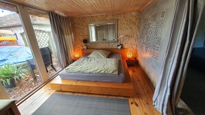 Ein Schlafzimmer mit Steinsturz, einem Bett mit Kopfteil, einem Nachttisch mit Lampe und Blick ins Freie.