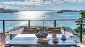 Ein Balkon mit Tisch für zwei Personen, mit Blick auf ein Gewässer, in dessen Ferne Boote und Inseln liegen.