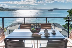 Un balcon avec une table dressée pour deux personnes, d’où l’on peut admirer un plan d’eau avec des bateaux et des îles au loin.