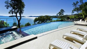 A infinity pool with clear blue water, surrounded by lounge chairs and a view of the sea and hills. - Shorelines 27 Hamilton Island - oceanviews, golf buggy and transfers (Hamilton Island)