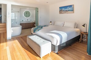 A modern bedroom with a large bed, a bench, a bedside table, a lamp, and a painting on the wall.