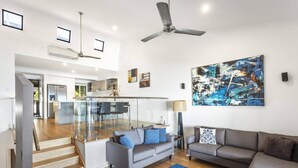 A modern living room with a grey sofa, a blue rug, and a ceiling fan. - Shorelines 27 Hamilton Island - oceanviews, golf buggy and transfers (Hamilton Island)
