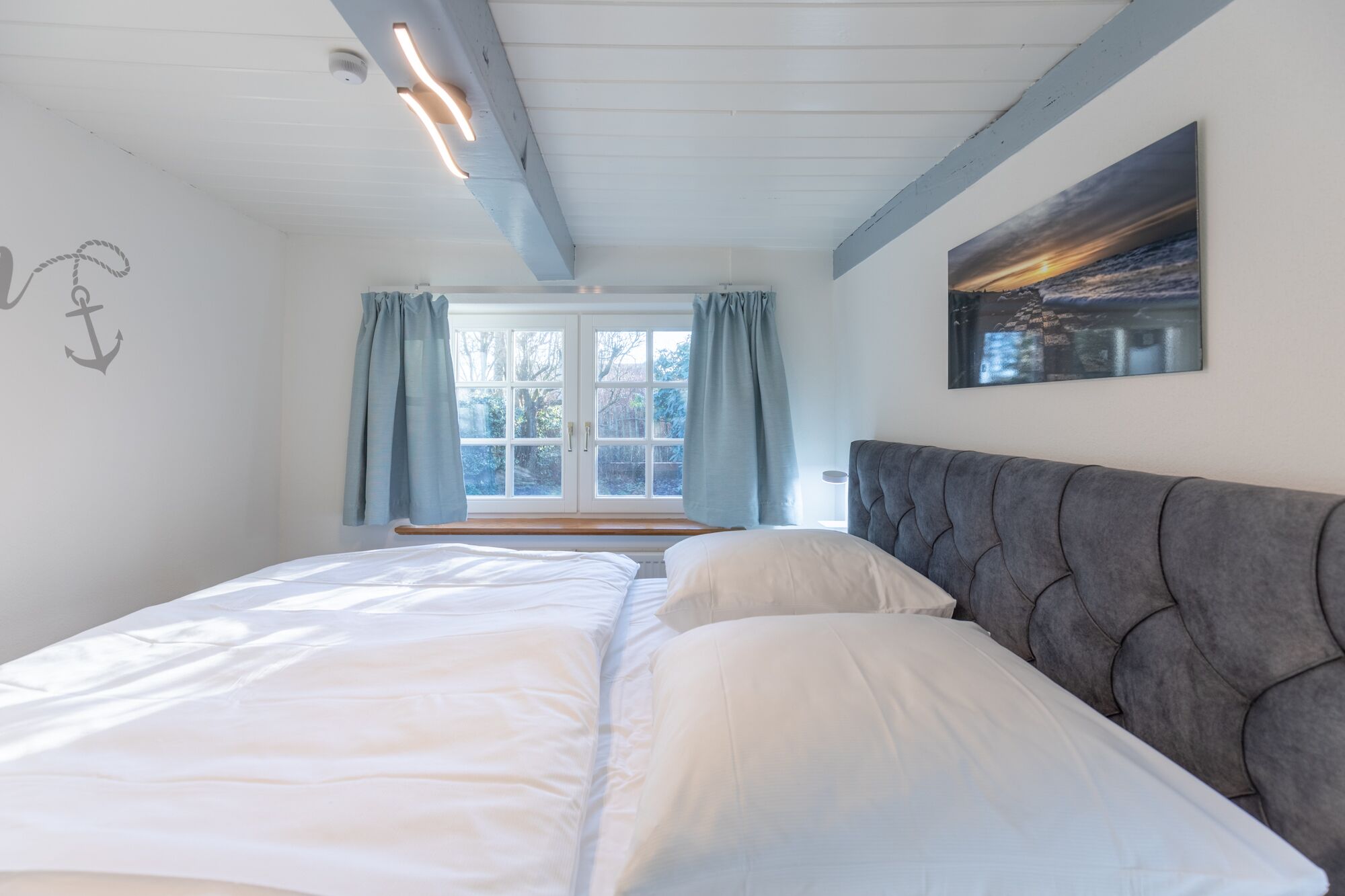 A bedroom with a bed, a window with curtains, a headboard, and a painting on the wall.