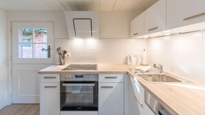 Moderni keittiö, jossa on valkoiset kaapit, sisäänrakennettu uuni, pesuallas ja ikkuna, josta avautuu näkymä tiiliseinälle.
