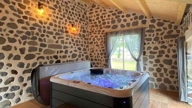 Ett rum med stenväggar, ett bubbelbad, trägolv och ett fönster med gardiner.