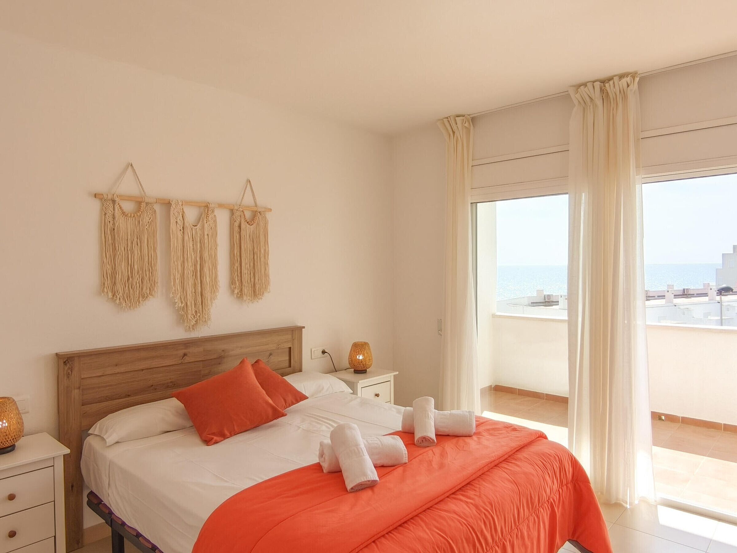 Een hotelkamer met een bed, nachtkastje, lamp en uitzicht op zee.