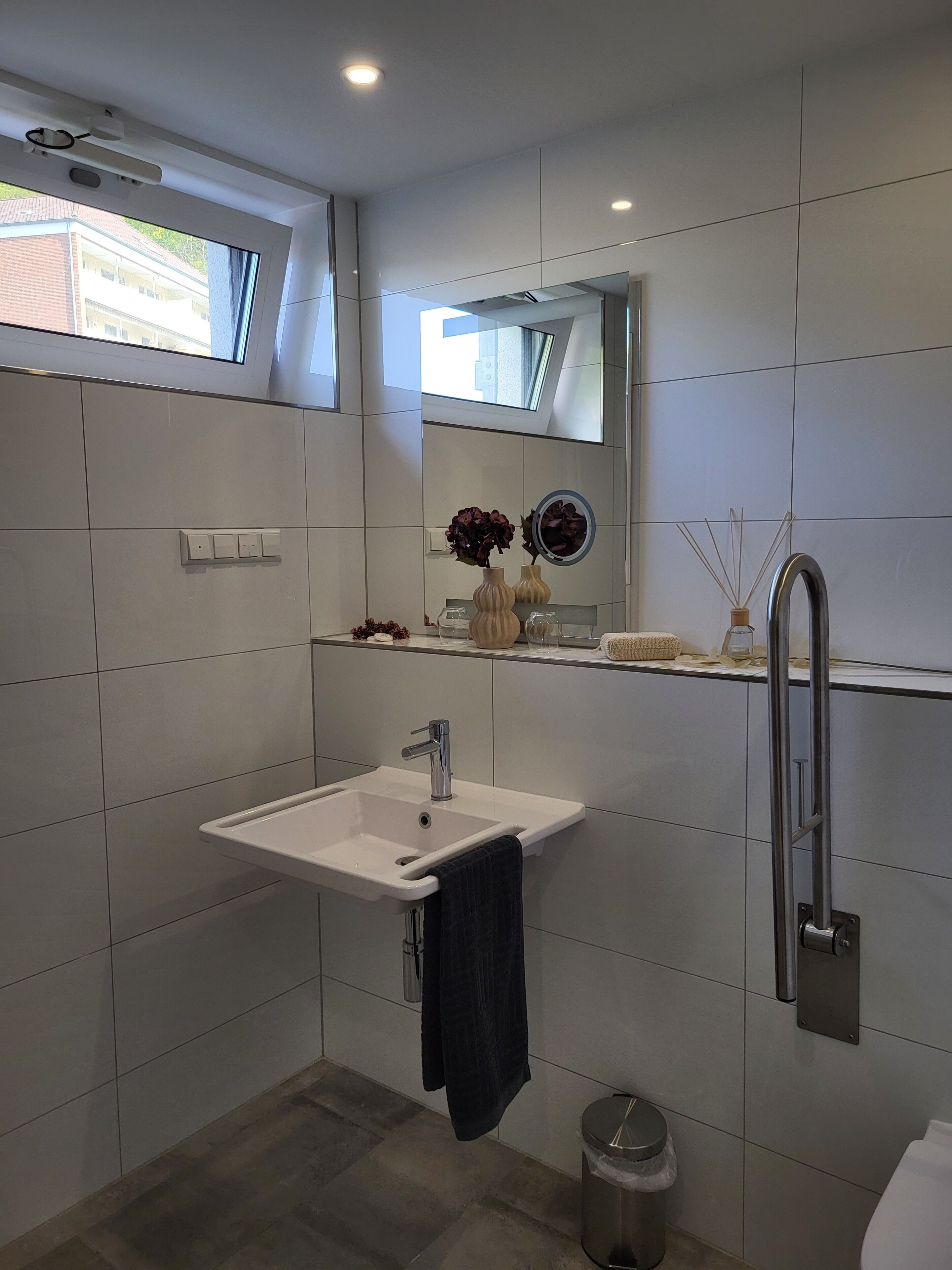 Un baño moderno con un lavamanos blanco, un espejo y un perchero para toallas.