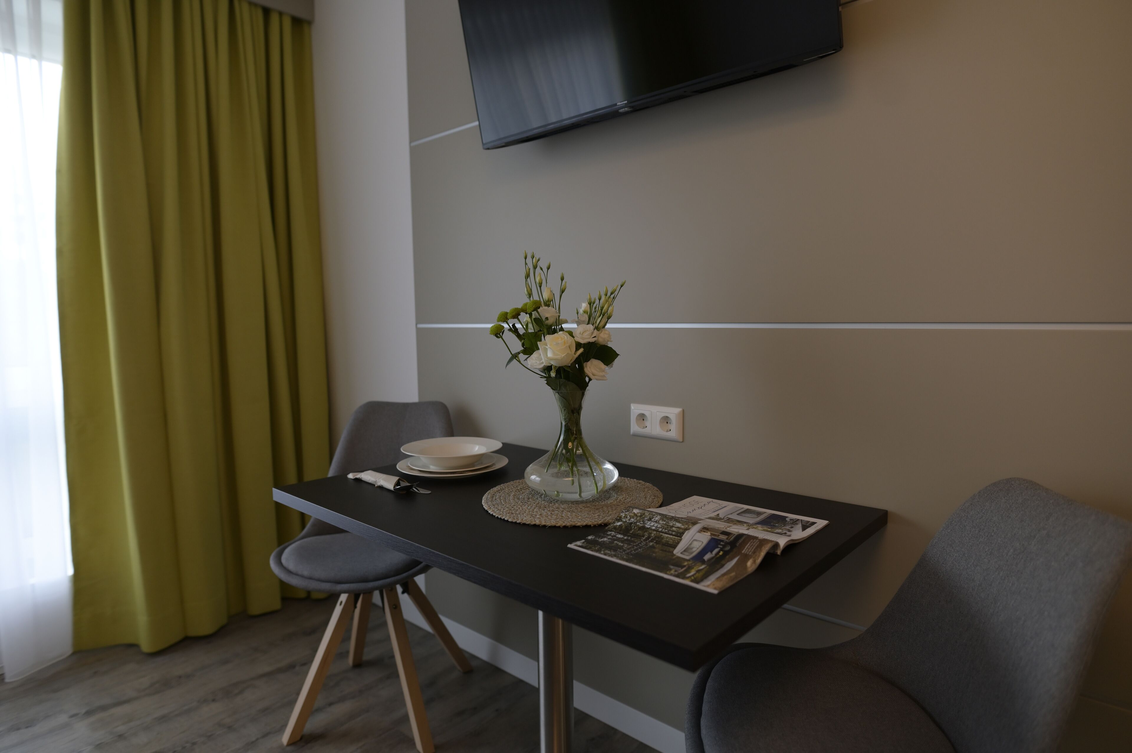 A modern dining area with a table, chairs, a vase with flowers, a placemat, and a magazine.