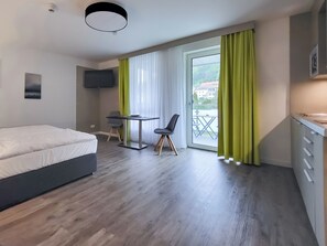 Una habitación de hotel moderna con cama, escritorio, silla, televisor y balcón con cortinas.