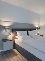 Quarto moderno com uma cama grande, duas mesas de cabeceira e luminárias fixadas na parede.