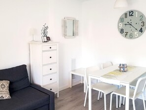 Une pièce moderne et minimaliste, avec une commode blanche, un canapé noir, une table à manger entourée de chaises blanches et une horloge murale.