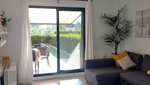 Un salon moderne avec un canapé gris, une grande porte-fenêtre coulissante donnant sur une terrasse extérieure et une plante en pot.