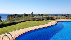Une piscine dotée d’une terrasse en bois et d’un escalier en métal, entourée de verdure et offrant une vue sur la mer.
