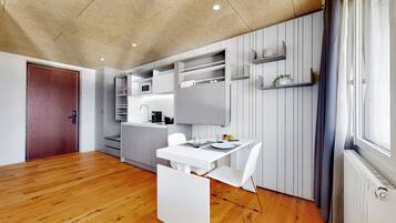 Una cocina moderna con electrodomésticos integrados, un comedor con mesa y sillas blancas, y suelo de madera.
