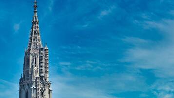 A historic cathedral with a tall spire, surrounded by traditional buildings and a clear blue sky.