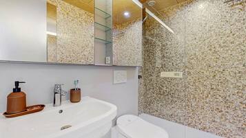 Un baño moderno con un lavamanos blanco, un espejo, una ducha con pared de azulejos y un inodoro.