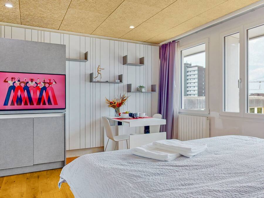 Una habitación de hotel moderna con una cama grande, un escritorio con una silla, un televisor montado en la pared y una ventana con vistas a la ciudad.