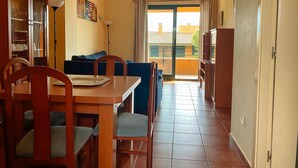 Un comedor con una mesa y sillas de madera, un sofá azul y vistas al exterior a través de un ventanal.